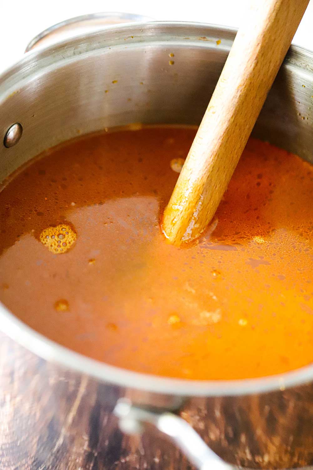 Shellfish stock in a large stock pan with a wooden spoon submerged into the liquid.