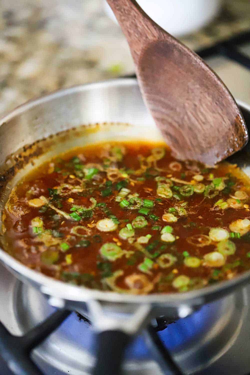 A small silver skillet filled with hot and sweet dipping sauce that is simmering and being stirred by a wooden spoon.
