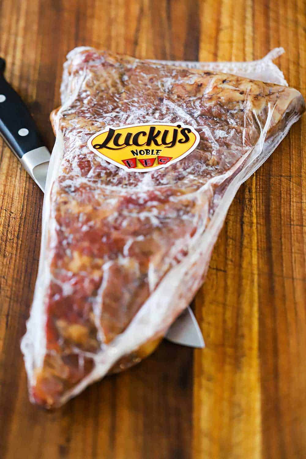 A package of Wagyu boneless beef short ribs sitting on a knife all on a wooden cutting board.