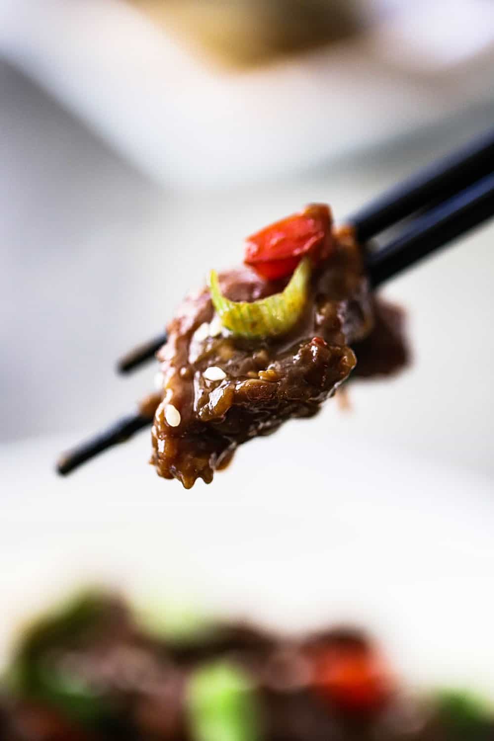 A pair of chop sticks holding up a piece of Mongolian beef.