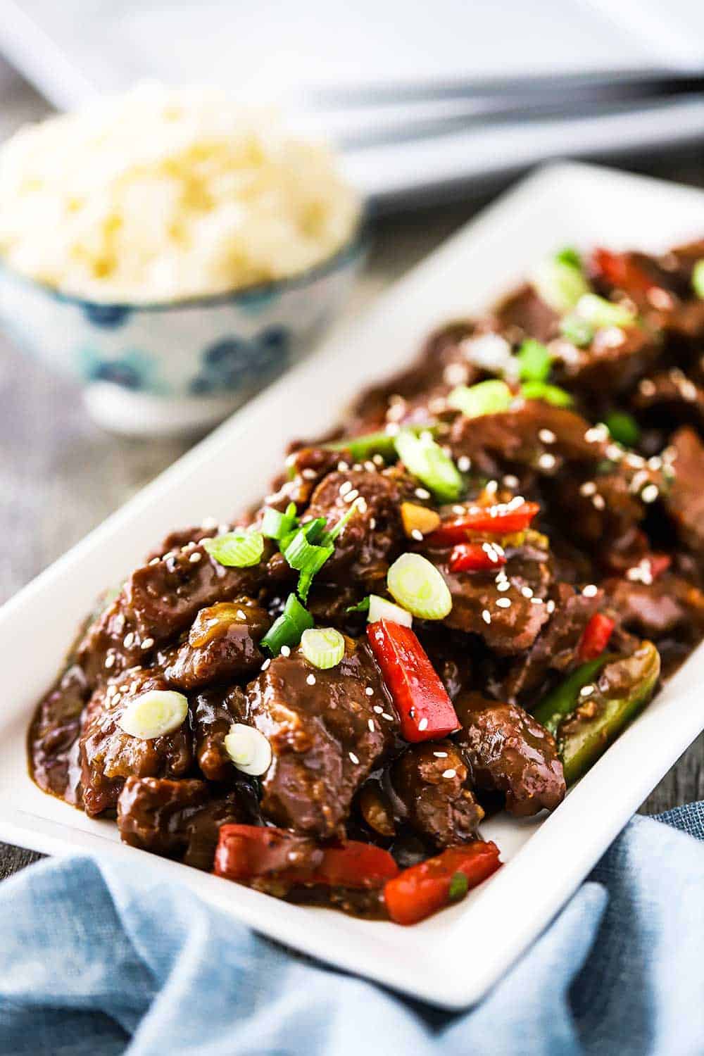 A white rectangular platter filled with prepared Mongolian beef and garnished with snipped chives and white sesame seeds.
