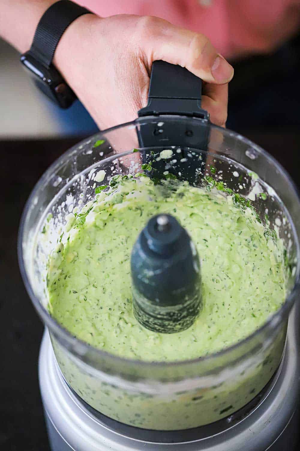 A bowl of a food processor that is filled with puréed avocado-lime dressing.