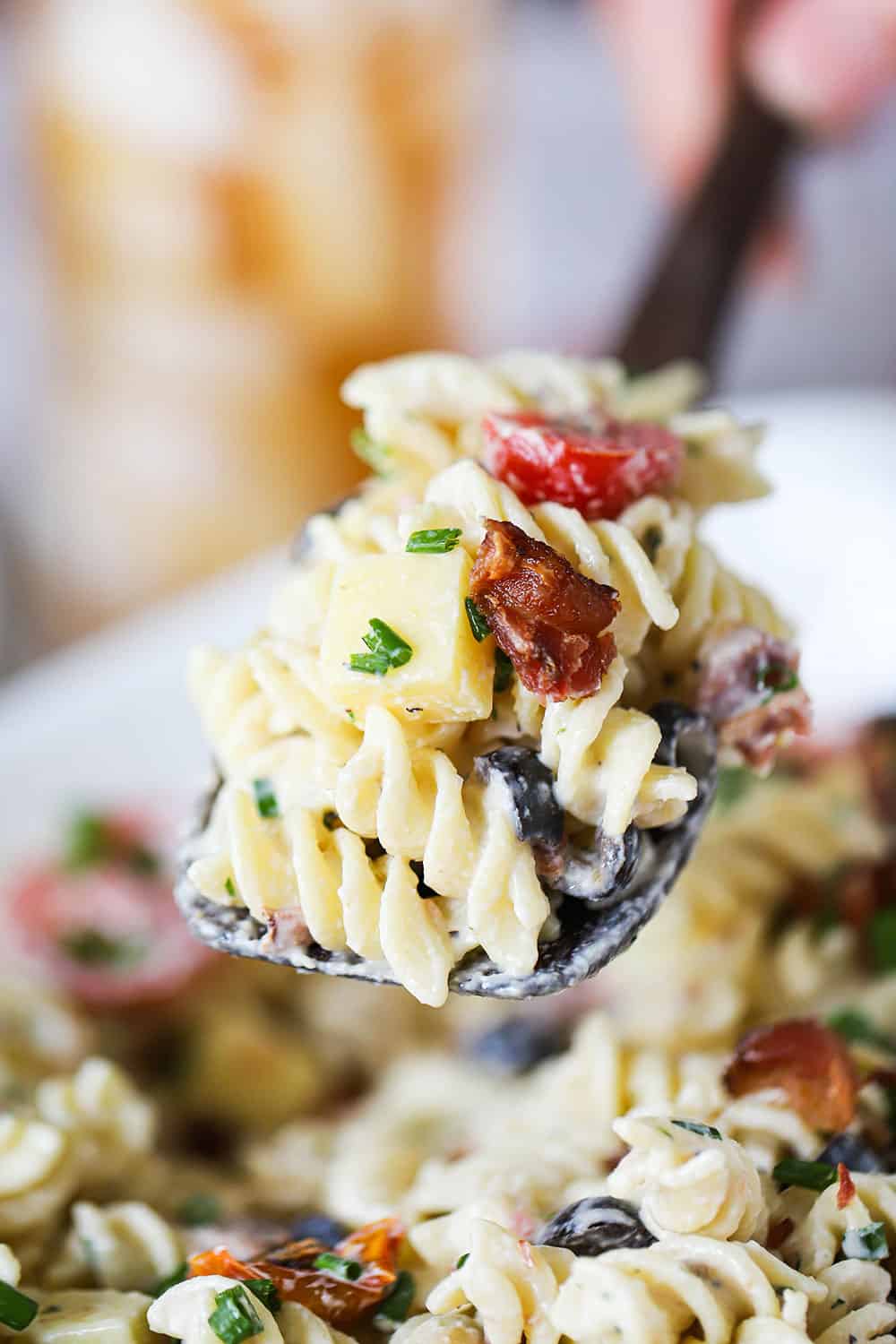 A large wooden spoon filled with Cheddar Bacon Ranch Pasta Salad over a bowl of the same.
