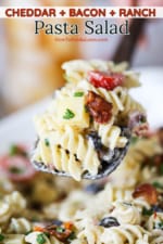 A large wooden spoon filled with Cheddar Bacon Ranch Pasta Salad over a bowl of the same.