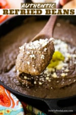 A wooden spoon lifting up a helping of refried beans over a pot of the same.