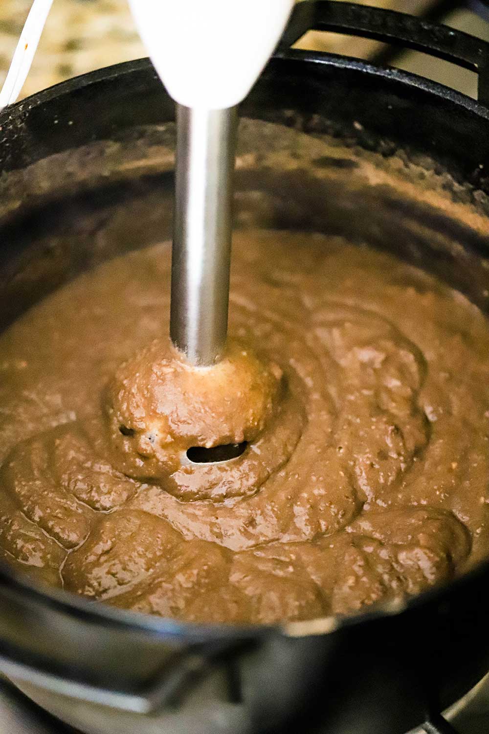 An emulsion blender plunged into a pot of cooked and puréed pinto beans.