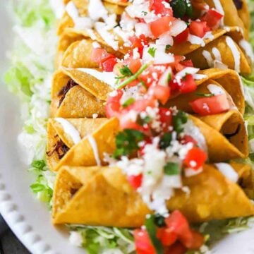 A row of cooked flautas on a bed of shredded lettuce all on a white oval platter.