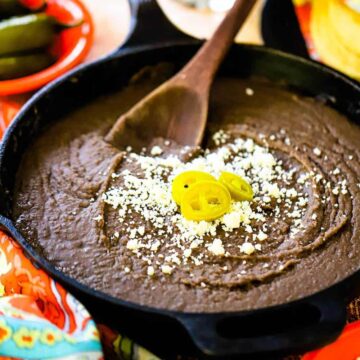 A cast-iron skillet filled with refried beans and topped with crumbled Cojita cheese and several jalapeno slices.