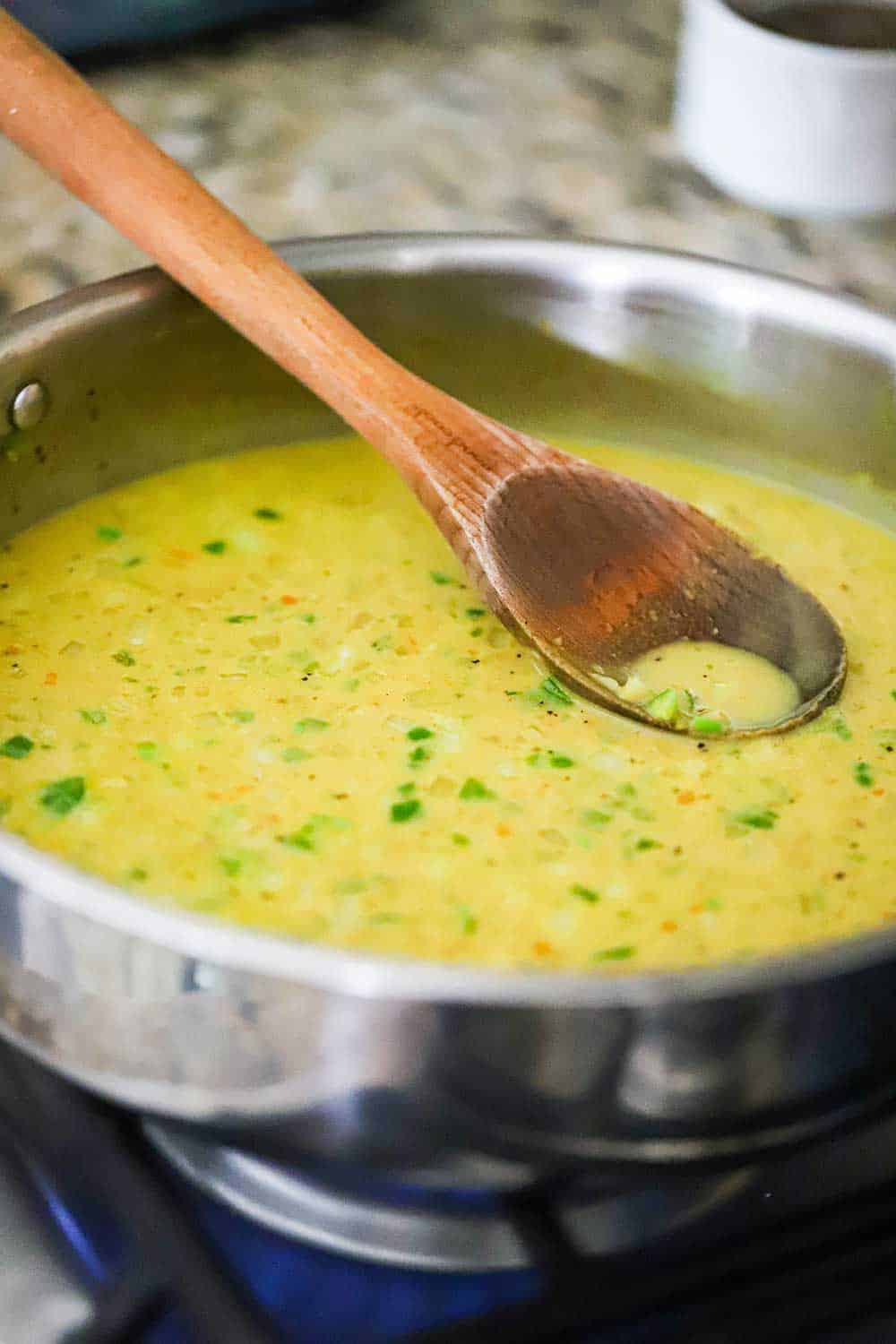 A skillet filled with a Jamaican curry sauce being stirred by a wooden spoon.