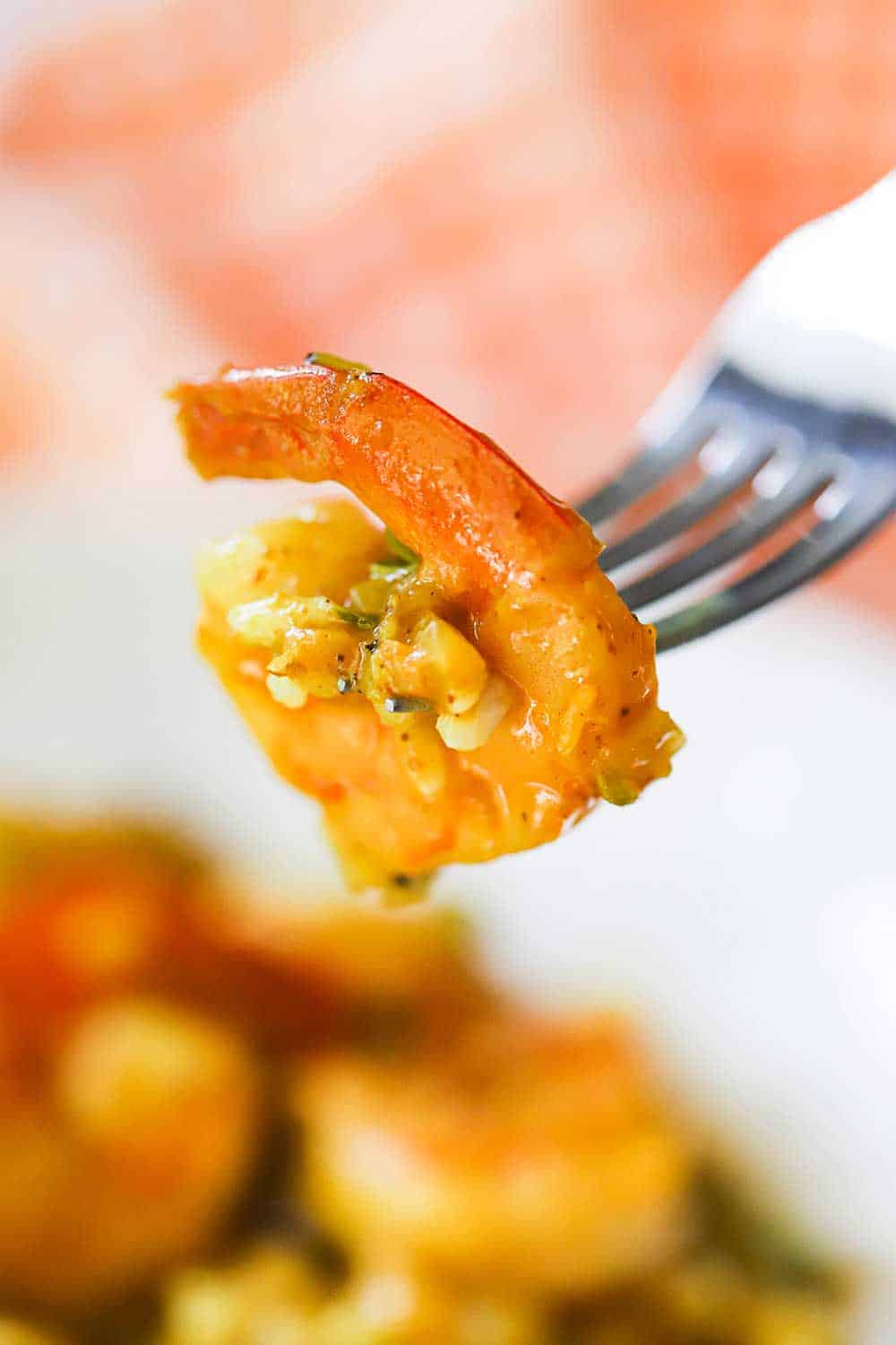 A fork holding up a shrimp that has been cooked in a Jamaican curry sauce.