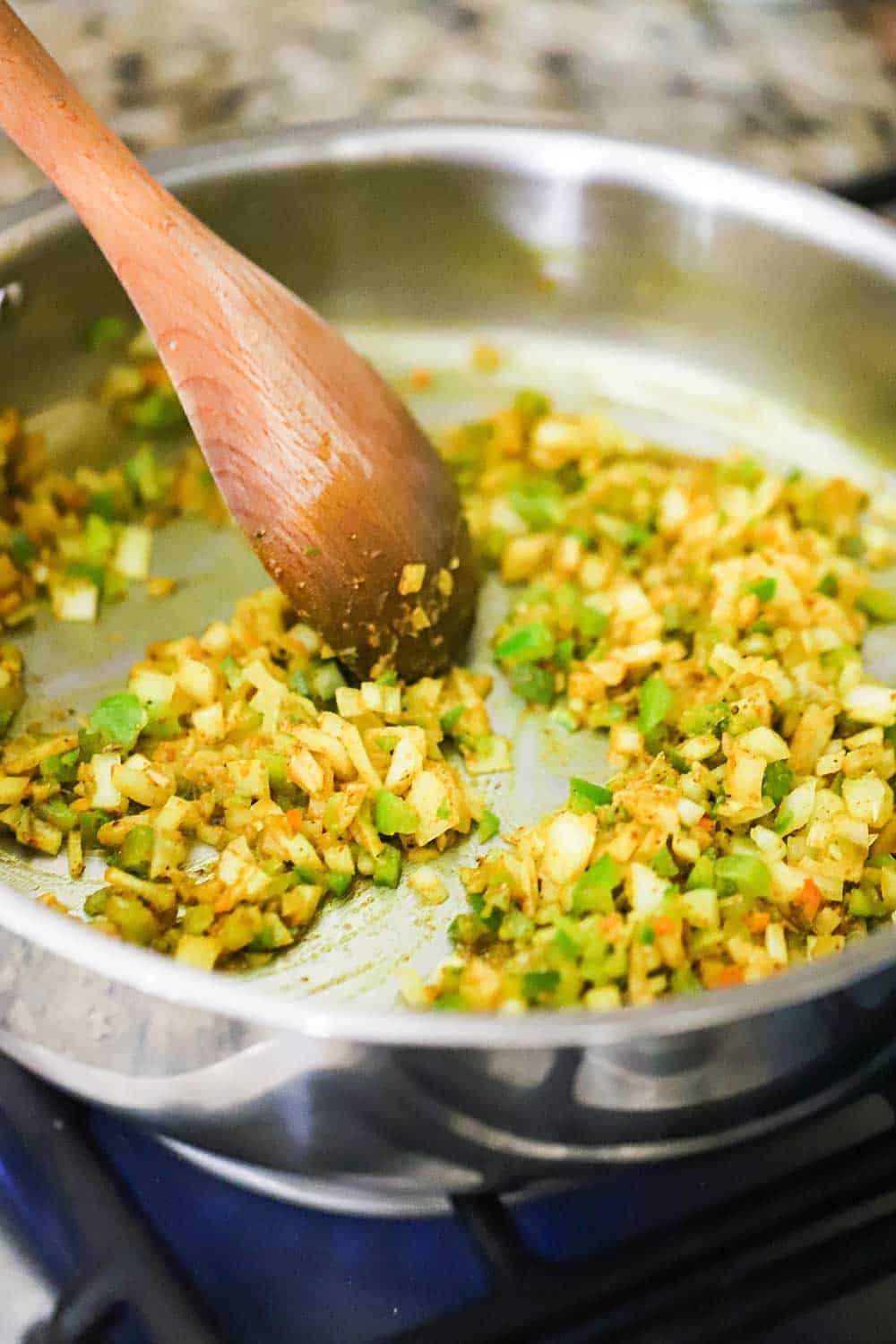 Chopped green bell peppers and onions being sautéd in a skillet of butter and curry powder.