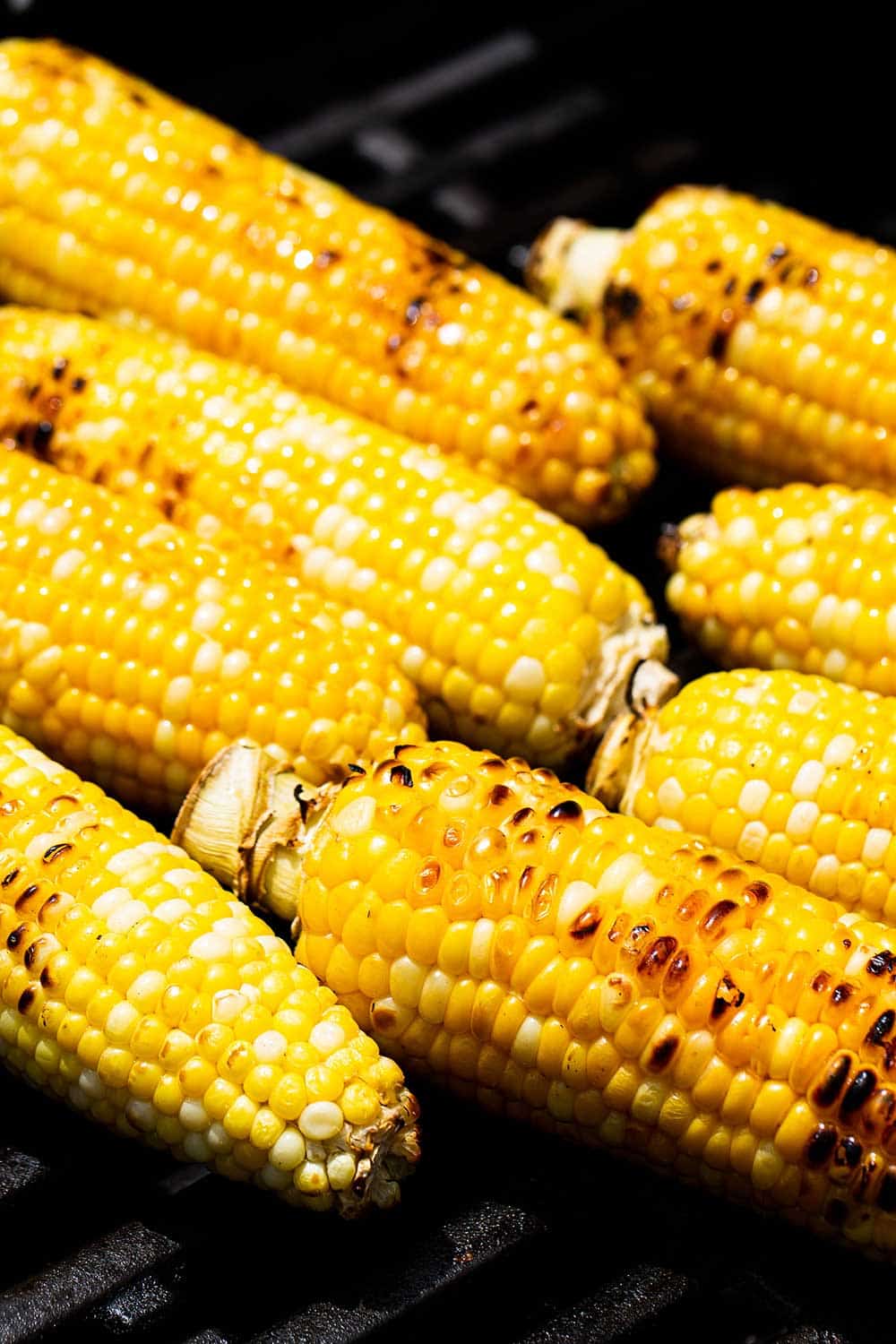 8 ears of corn being grilled on a gas grill.