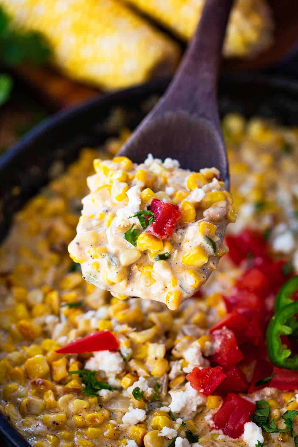 A wooden spoon lifting up a helping of Mexican cream corn from a skillet.