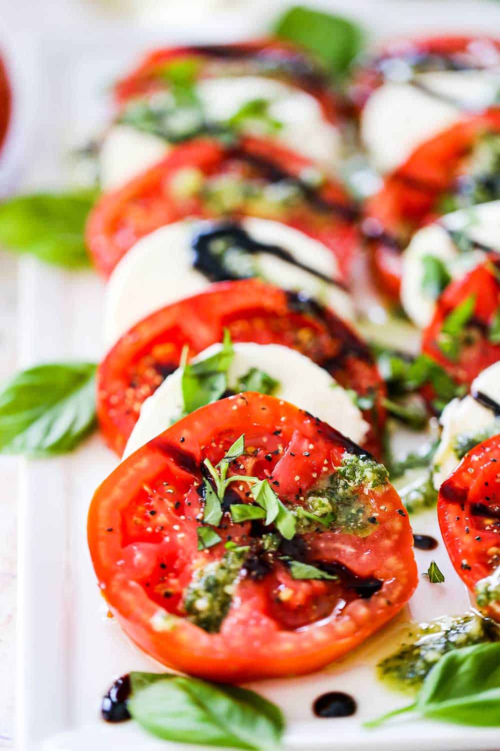 A platter of caprese salad that has been drizzled with pesto sauce and a balsamic glaze and topped with freshly chopped basil.