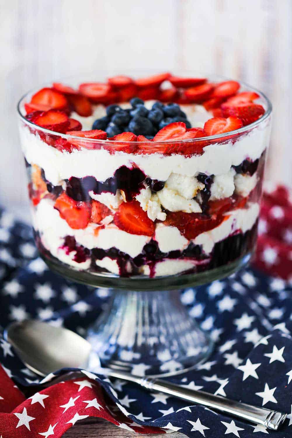 A red, white, and blue trifle sitting on top of a patriotic table cloth next to a large silver serving spoon.
