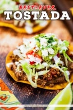 A crispy flat corn tortilla topped with layers of refried beans, taco meat, lettuce, tomatoes, and cream.