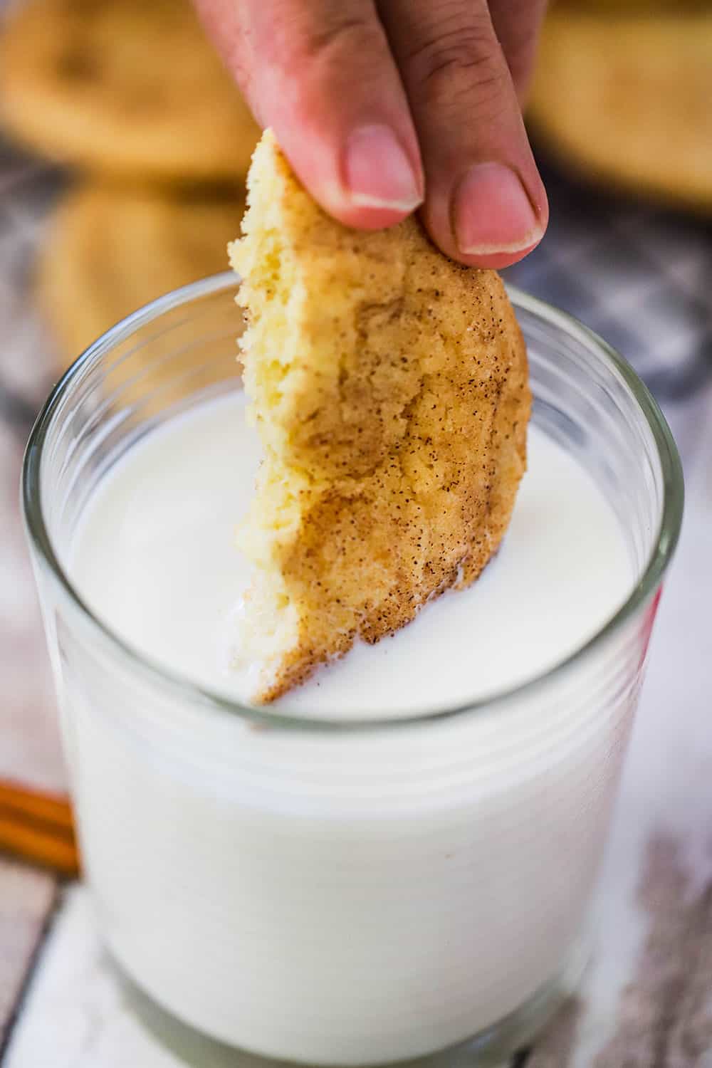 A hand dipping a cookie that has been halved into a glass of milk.