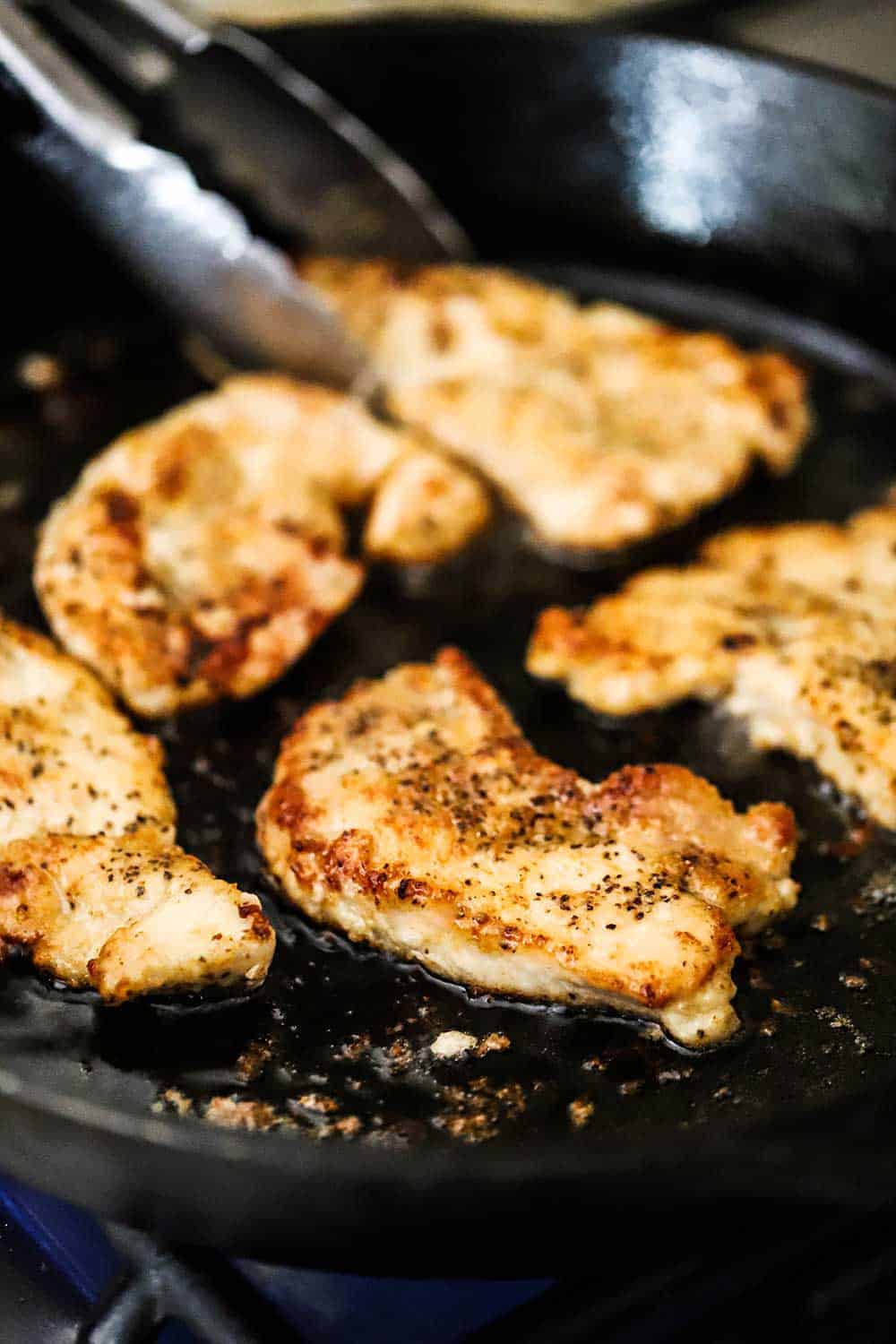 5 thin pork cutlets that are being pan-fried in a large black cast-iron skillet.