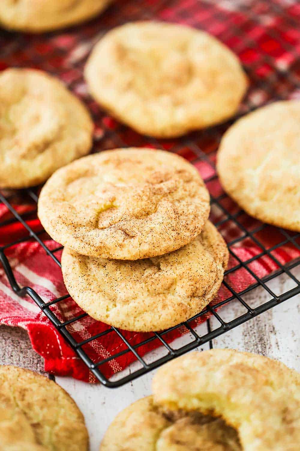 A baking rack topped with snickerdoodle cookies all on top of a red-checkered napkin.