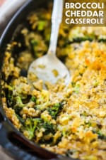 A large oval baking dish filled with broccoli casserole with part of it missing and a large serving spoon sitting in the dish.