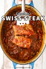 A metal spatula holding up two steak fillets covered in a red tomato sauce directly over an oval Dutch oven filled with Swiss steak.