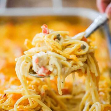 A spoon lifting a helping of chicken spaghetti out of a large lasagna pan.