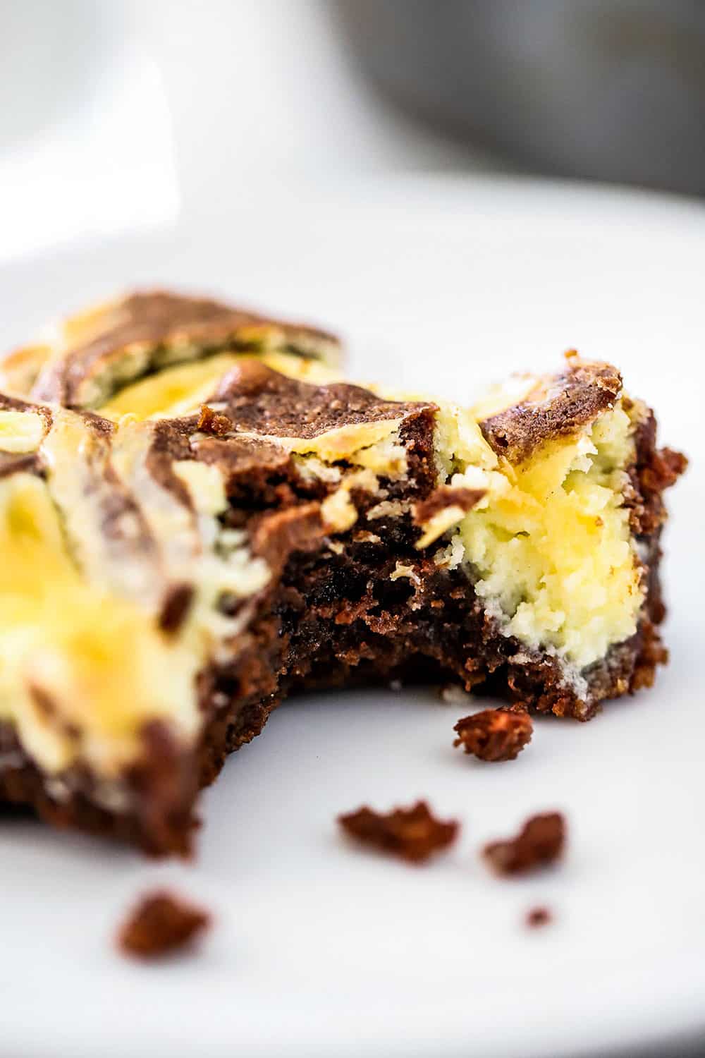 A chocolate and cheese cake brownie sitting on a white dessert plate with a bite taken out of it.