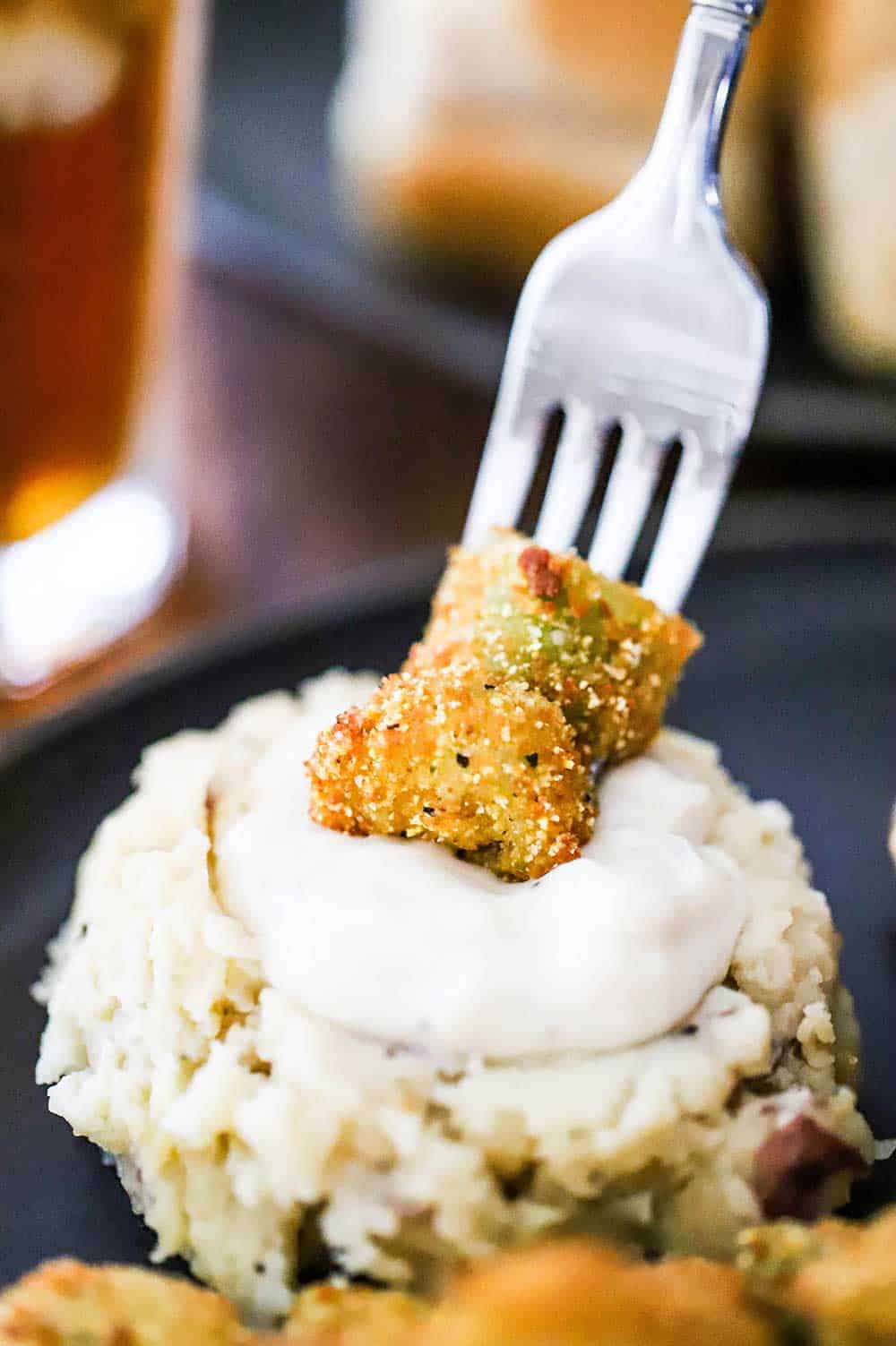 A fork with a couple of pieces of okra stuck on it being plunges into mashed potatoes with gravy.