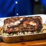 A person holding a large steel roasting pan filled with a roasted pork loin sitting on top of roasted apples and fennel.