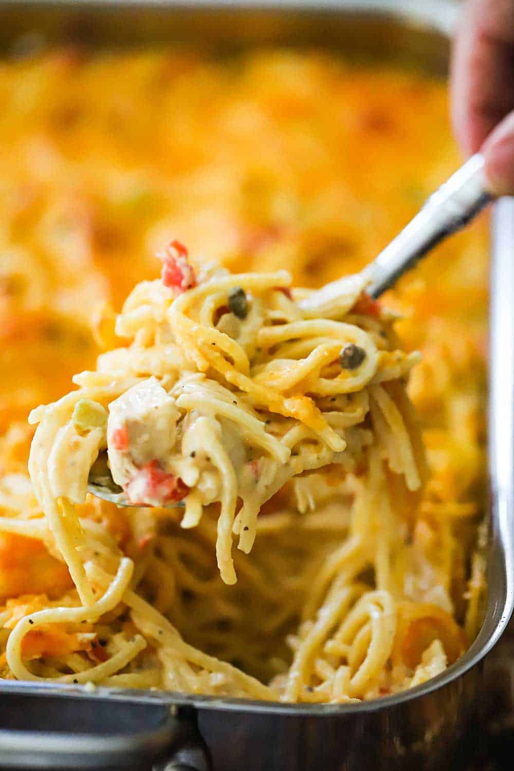 A spoon lifting a helping of chicken spaghetti out of a large lasagna pan.