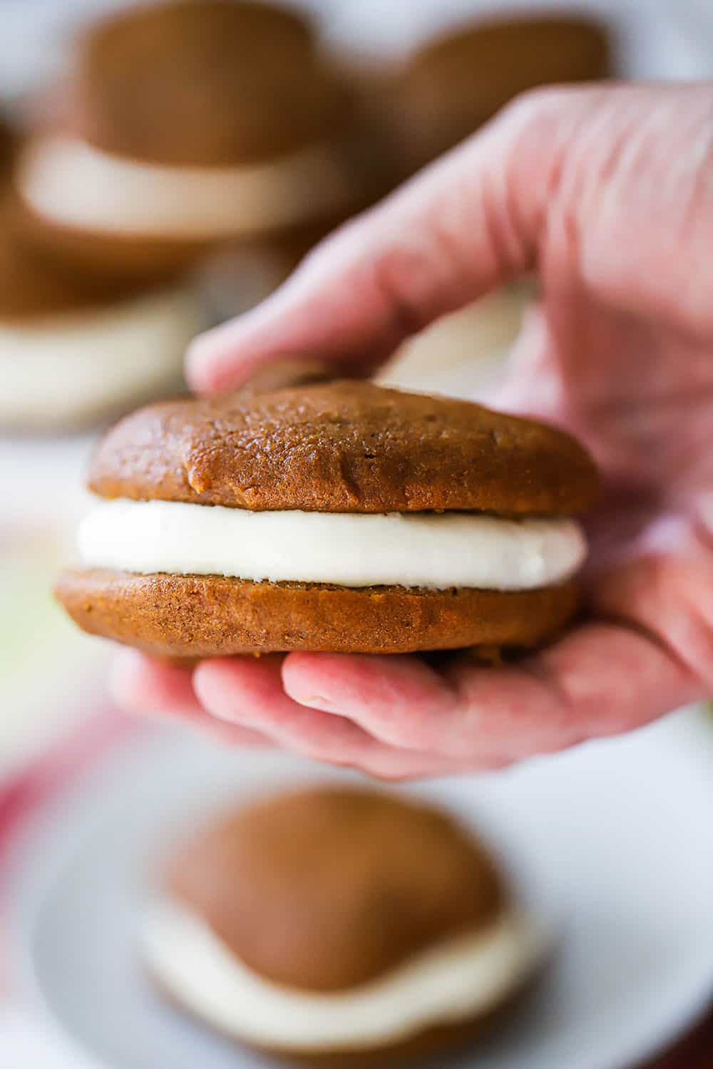 A hand holding a pumpkin whoopi pie filled with cream cheese filling.