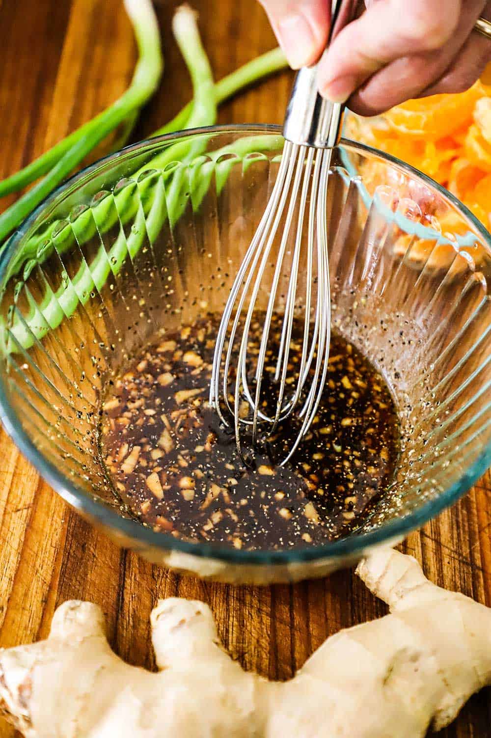 A whisk in a glass bowl filled with a marinade for chicken for a Chinese chicken salad.