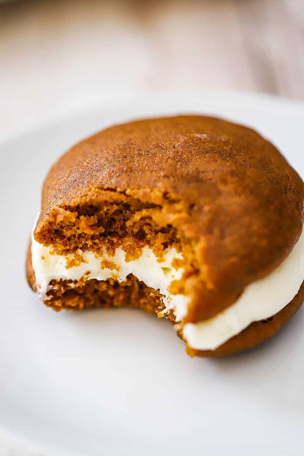 A pumpkin whoopie pie with a bite taken out of it sitting on a white dessert plate.