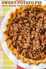 A sweet potato pie in a pie crust with fluted edges sitting in a white pie dish on an autumnal place setting.