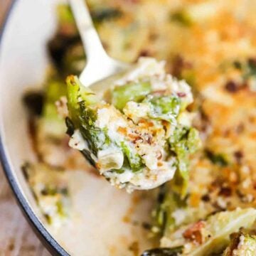 A person lifting up a spoonful of baked Brussels sprouts in a cream sauce out of an oval baking dish.