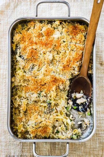 A large lasagna pan filled with turkey tetrazzini with a portion removed and a wooden spoon in its place.
