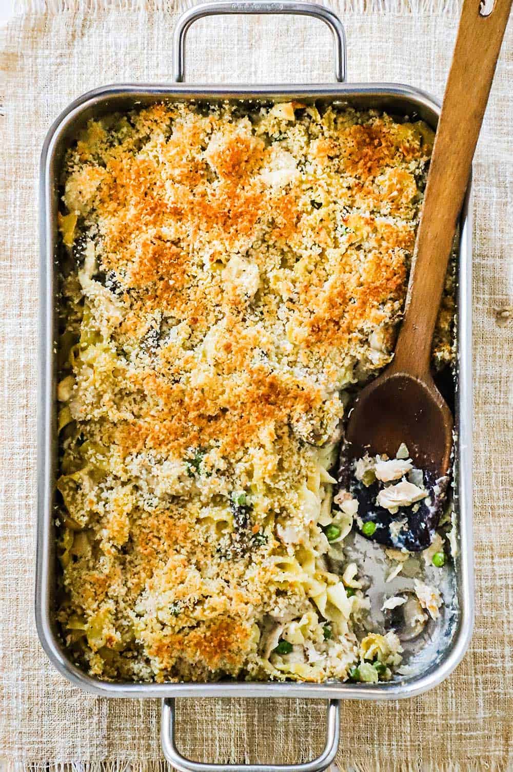 A large lasagna pan filled with turkey tetrazzini with a portion removed and a wooden spoon in its place.