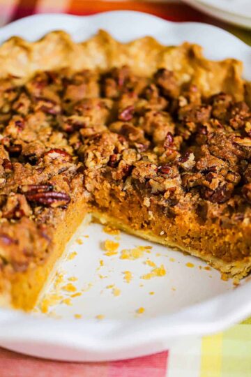 A sweet potato pie with pecan topping in a white pie dish with a large slice missing on one side of the dish.