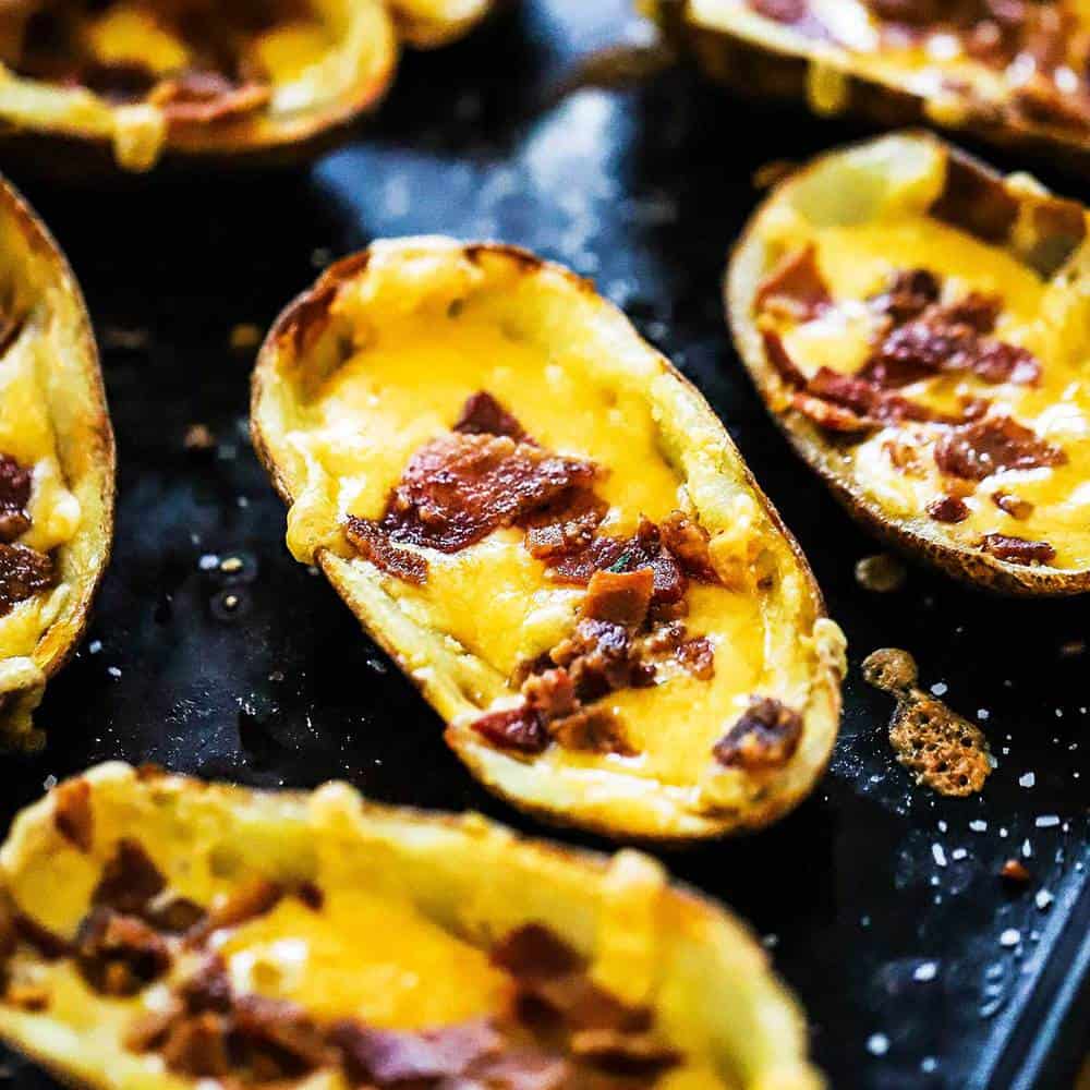A black baking sheet filled with loaded potato skins.