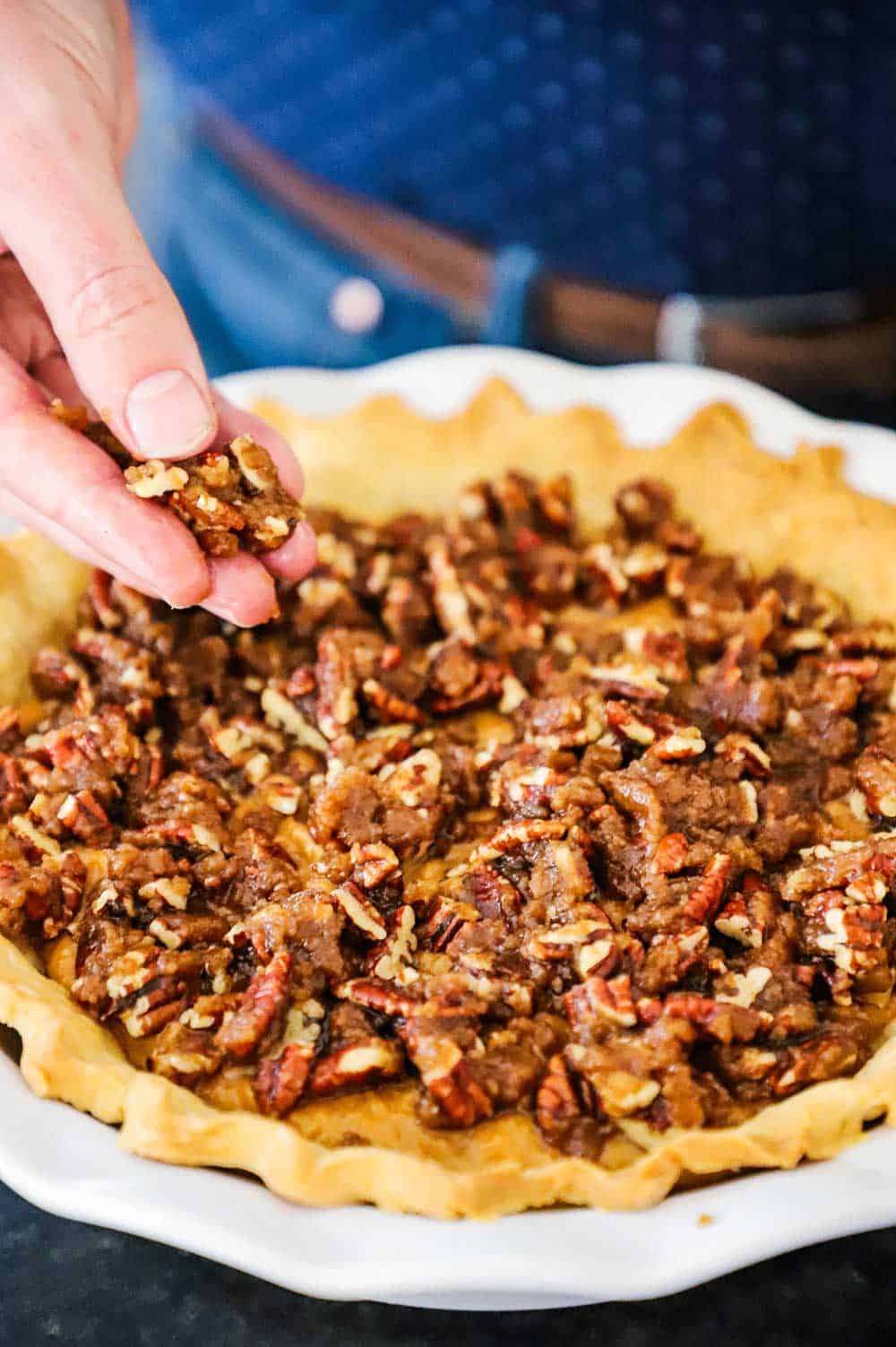 A person placing a pecan streusel mixture on top of a sweet potato pie filling in a pie dish.