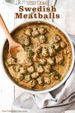 A large stainless steel skillet filled with Swedish meatballs and wooden spoon.