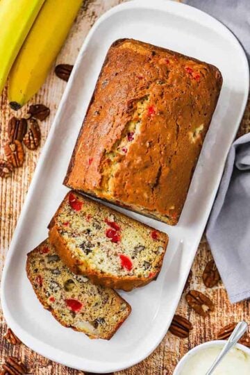 A loaf of banana nut bread with a couple slices that have been cut on a rectangular white serving dish.