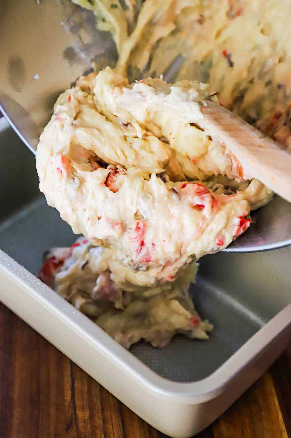 Bread batter being transferred from a mixing bowl into a metal loaf pan.