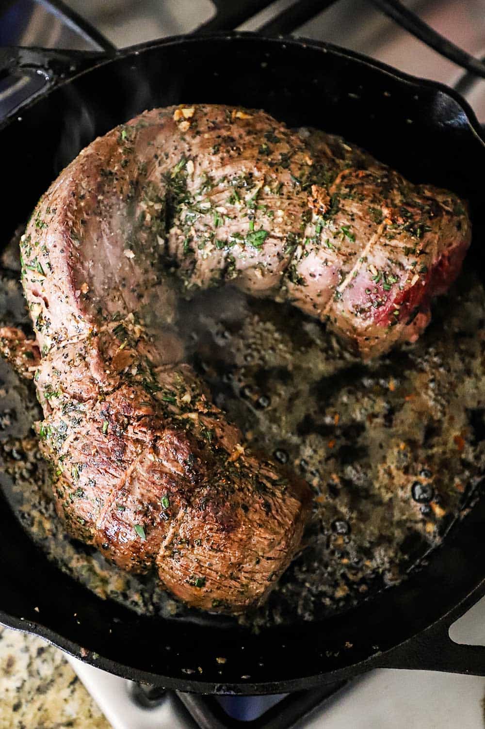 A large beef tenderloin roast that has been seared in a large black cast-iron skillet.