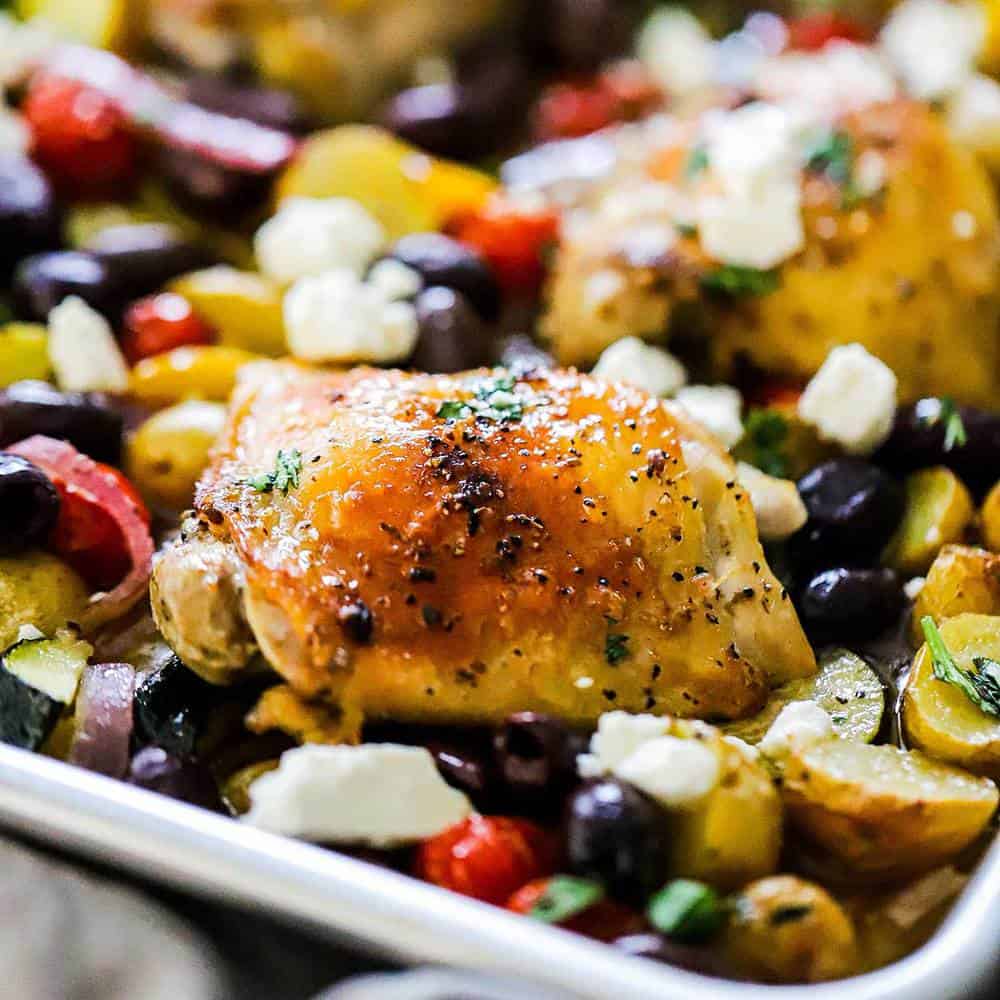 A cooked chicken thigh in a sheet pan surrounded by roasted vegetables.