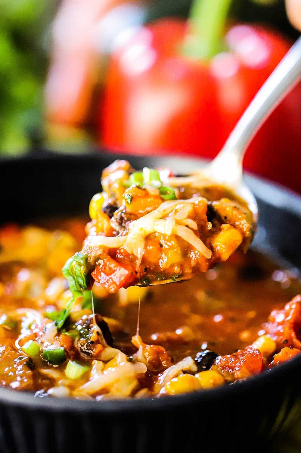 A spoon lifting out of a bowl filled with vegetable chili with black beans.