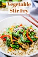 A white circular plate filled with vegetable stir-fry with brown chop sticks sitting on the side of the bowl.