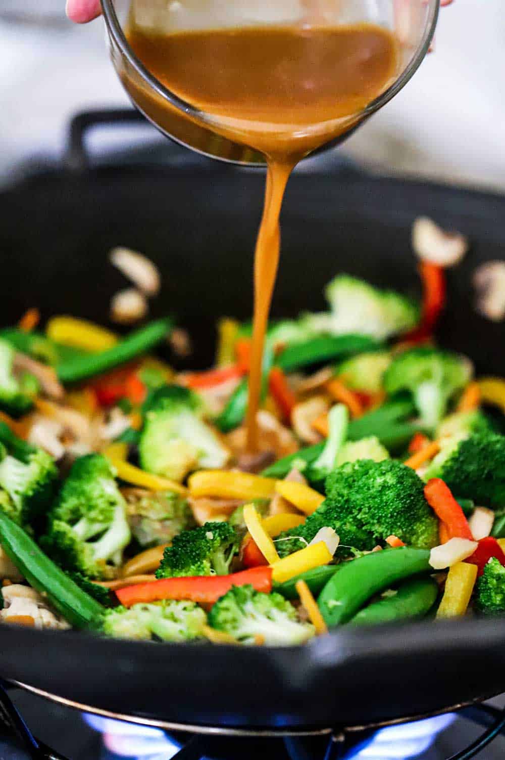 An Asian stir-fry sauce being poured into a wok filled with vegetable stir-fry.