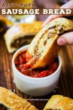 A person dipping a slice of sausage into a small white bowl of marinara sauce.