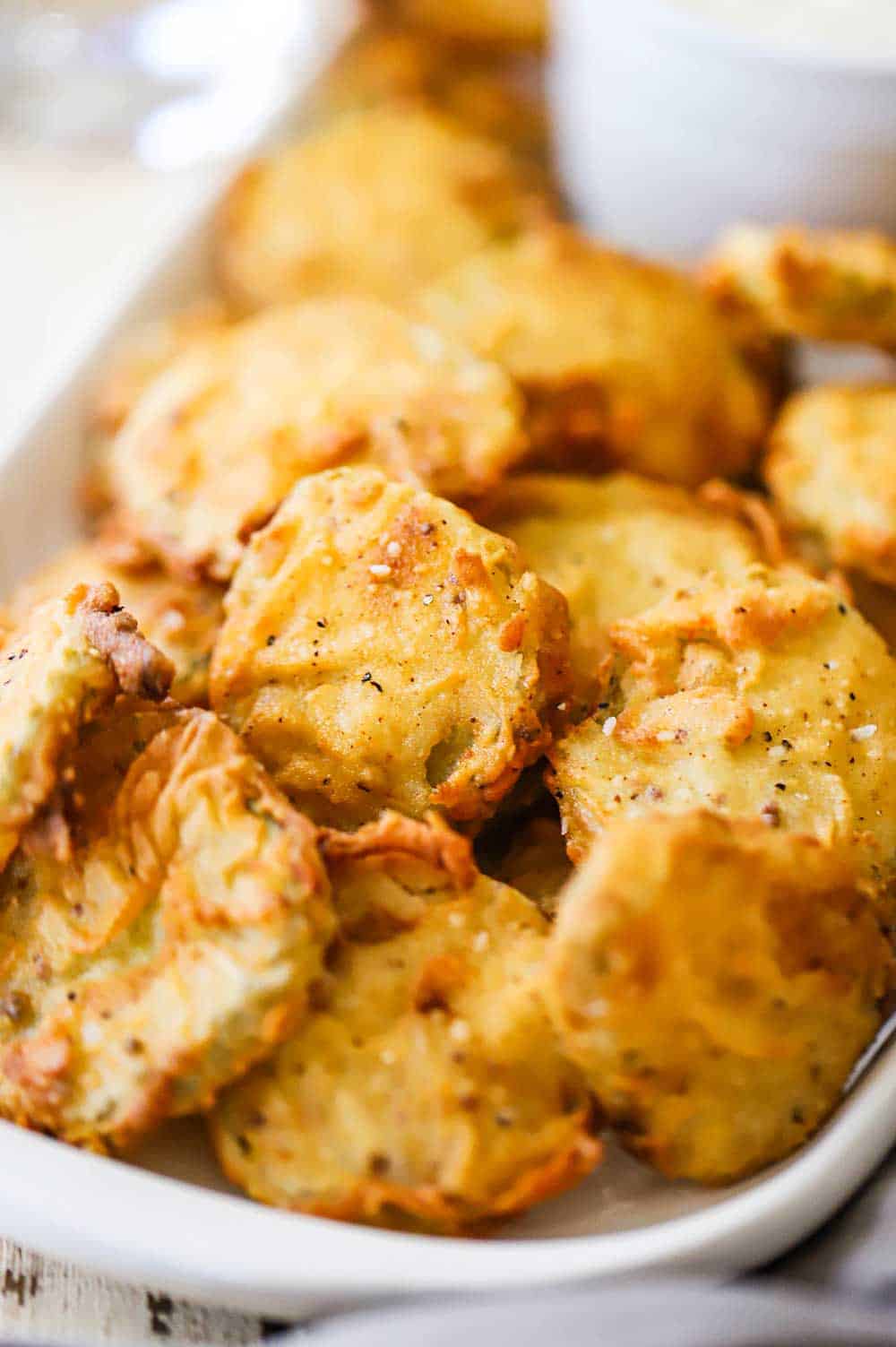 A rectangular platter filled with crispy fried pickles stack on top of each other.